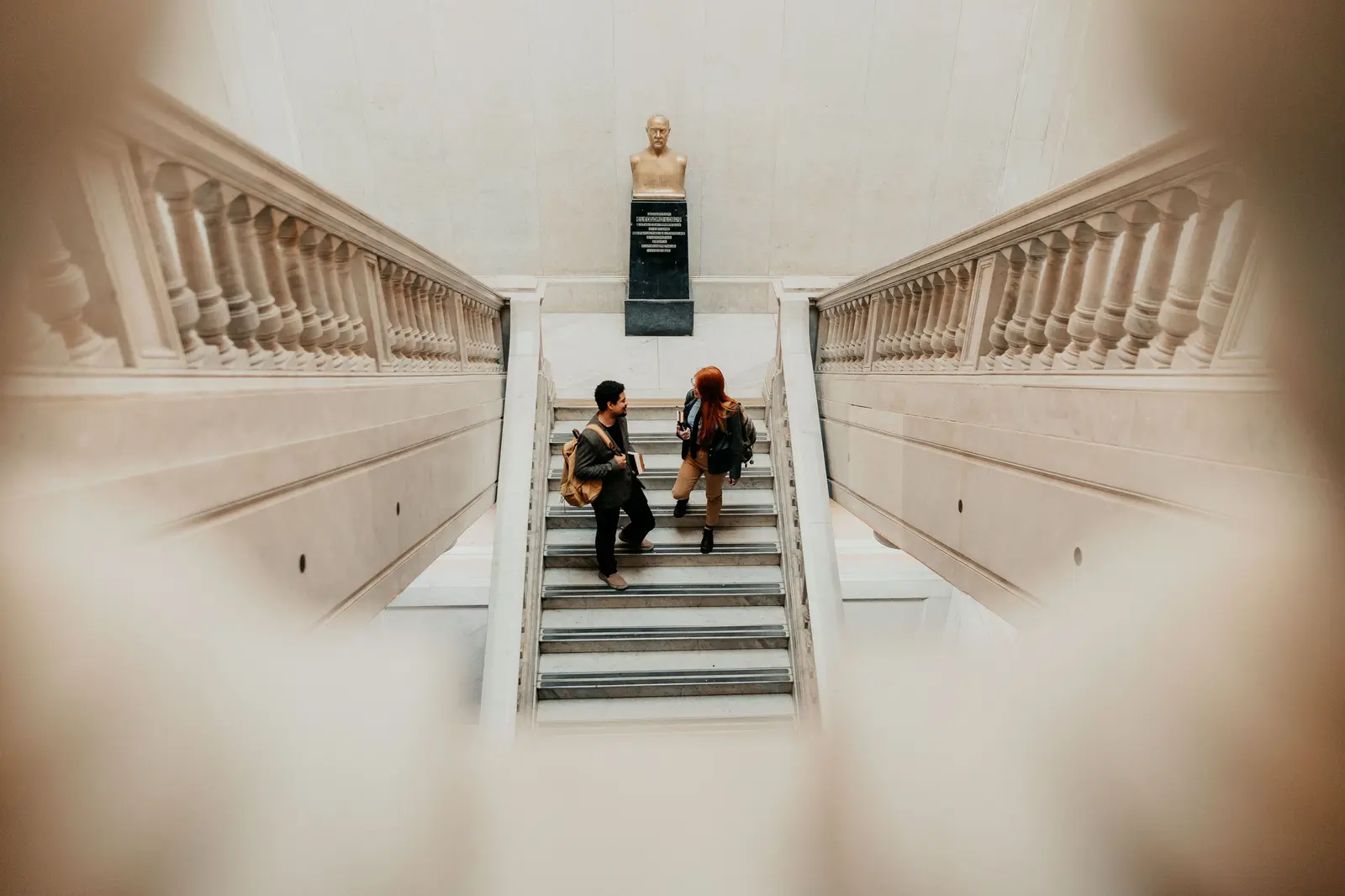 Two students talking on a grand staircase with a bust in Buenos Aires university.