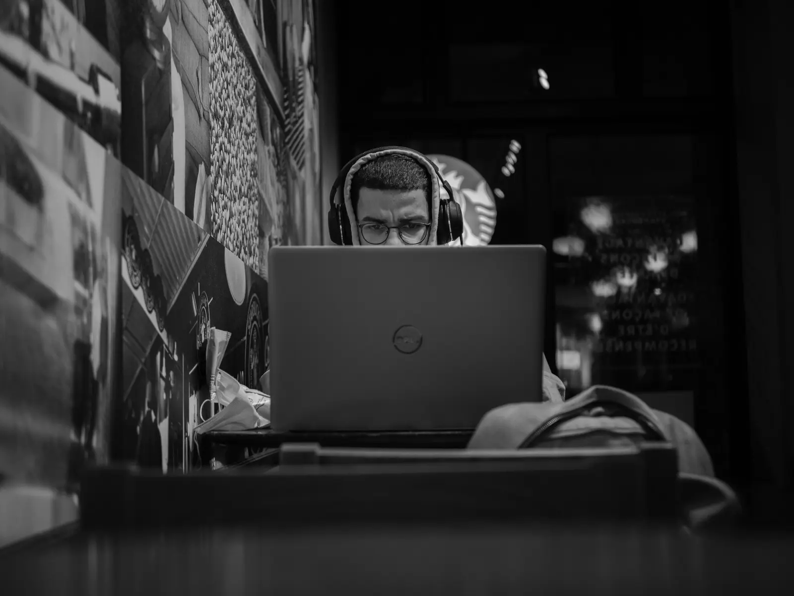 The best coworking spaces in Montreal Black and white photo of a man working remotely in a Montreal cafe using his laptop and headphones.