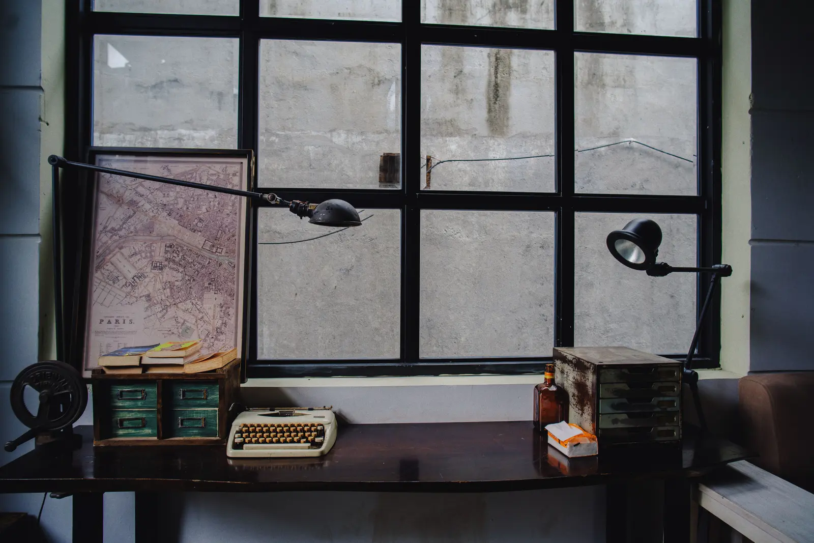 A vintage office desk setup featuring a typewriter, Paris map, and classic decor by a window.