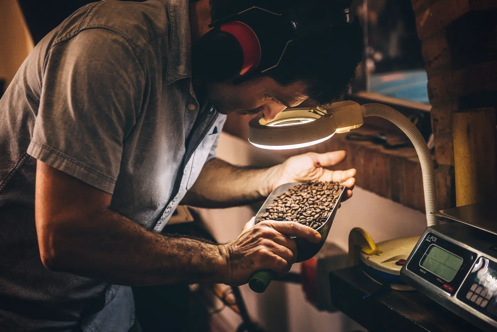 The best cafés to work from in Playa Del Carmen A man carefully inspects coffee beans under a lamp, showcasing the artisan process in Playa del Carmen.