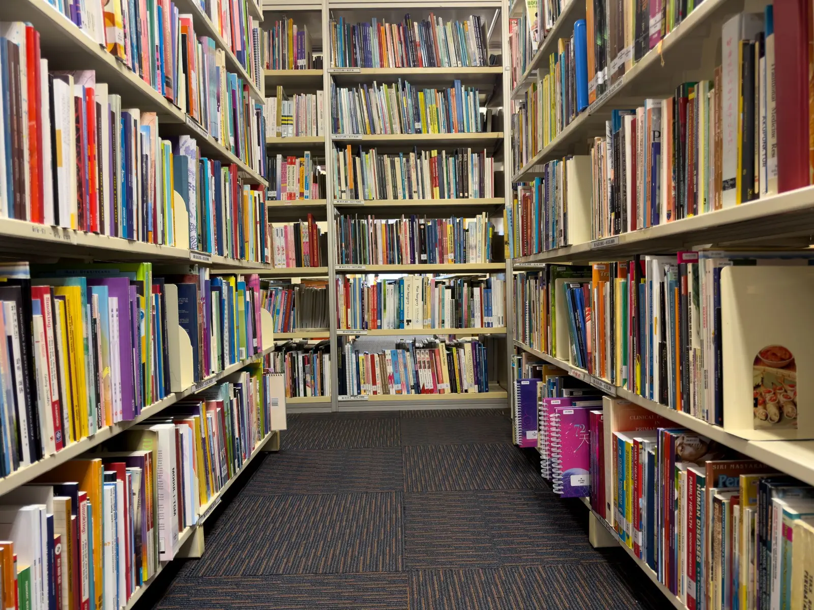 The best libraries to work and study in Kuala Lumpur Vibrant aisle of a library in Kuala Lumpur, filled with diverse books and educational resources.