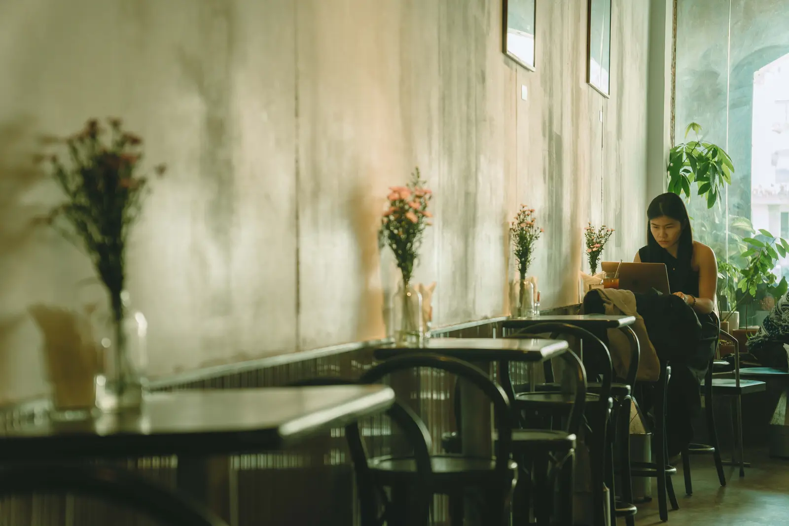 The best cafés to work from in Ho Chi Minh City A woman working on her laptop in a cozy cafe with elegant floral decor in Ho Chi Minh City.