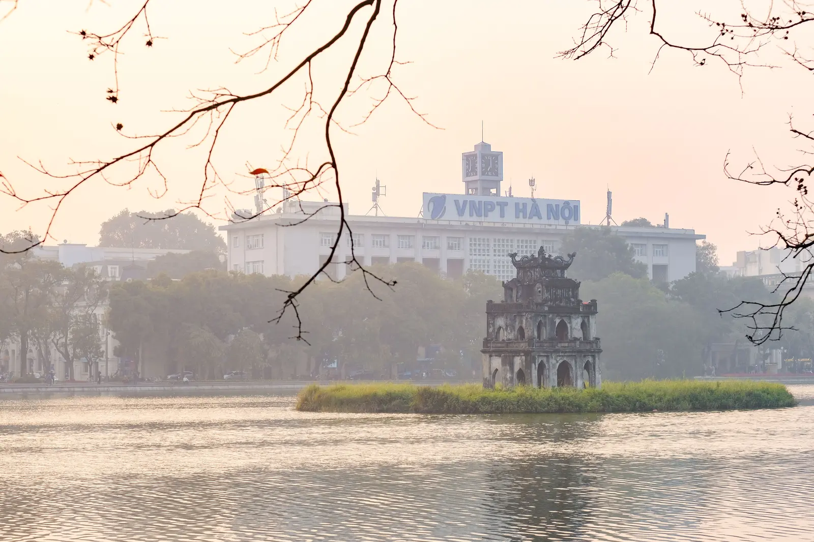 A scenic view of Turtle Tower on Hoan Kiem Lake surrounded by lush greenery in Hanoi, Vietnam.